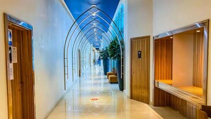 A hotel corridor with a reflective floor, wooden doors, and a blue ceiling design.