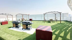 Terraço no telhado com grama sintética, duas churrasqueiras, área de estar ao ar livre e pérgulas que oferecem sombra.