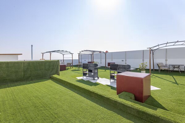 A rooftop terrace with artificial grass, outdoor furniture, and a barbecue area.