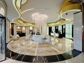 A hotel lobby with a central seating area, a reception desk, and a large chandelier.