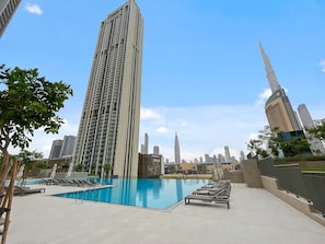 Un área de piscina en la azotea con sillas de descanso y vistas a edificios altos, incluyendo un rascacielos destacado.