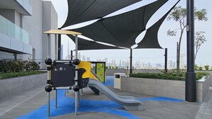 Um parquinho ao ar livre com escorregador e estrutura de escalada, cercado por edifícios modernos e vista para o horizonte da cidade.