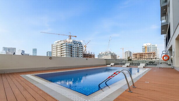Piscina no terraço com deck de madeira, rodeada por edifícios altos e guindastes de construção.