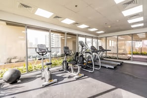 A gym with exercise equipment, large windows, and a view of buildings.