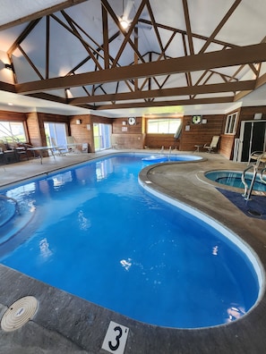 Ein Poolbereich mit mehreren Schwimmbecken, Liegestühlen und Holzvertäfelungen.
