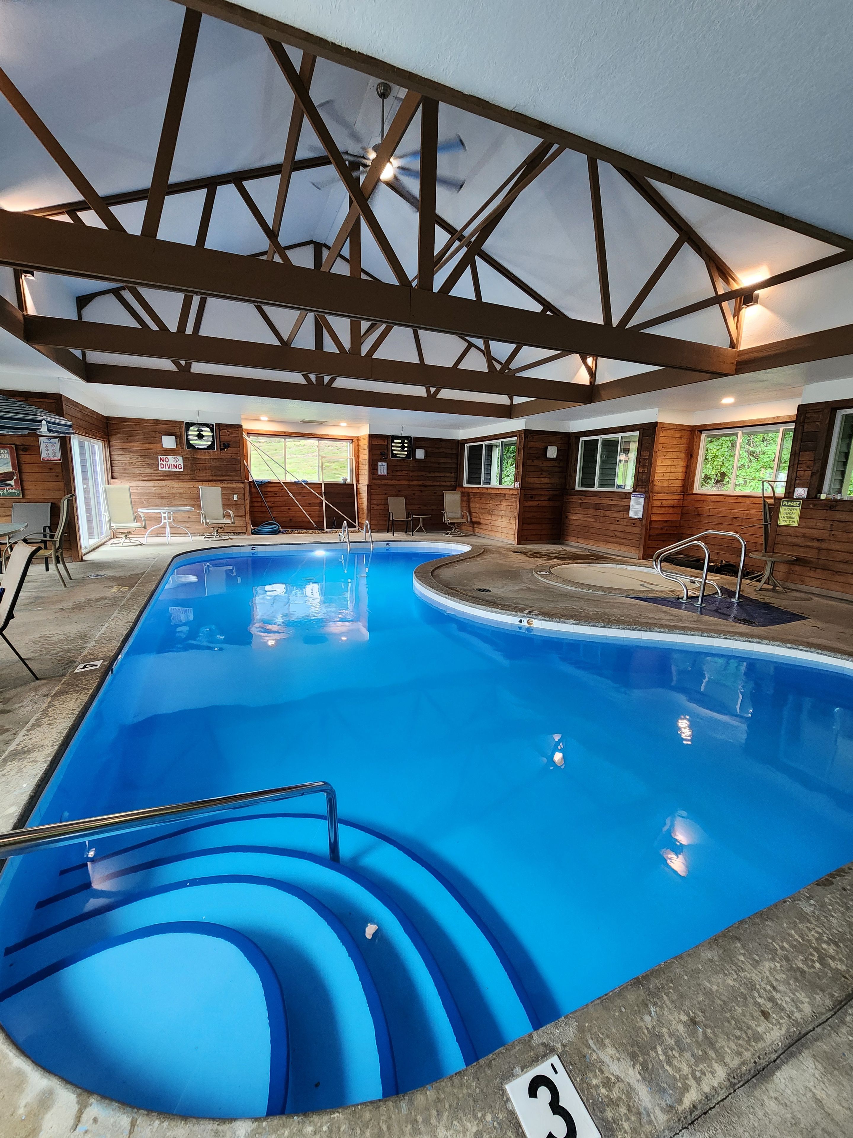 Une piscine intérieure avec un revêtement intérieur en bois, un ventilateur de plafond et un panneau indiquant qu’il est interdit de plonger.