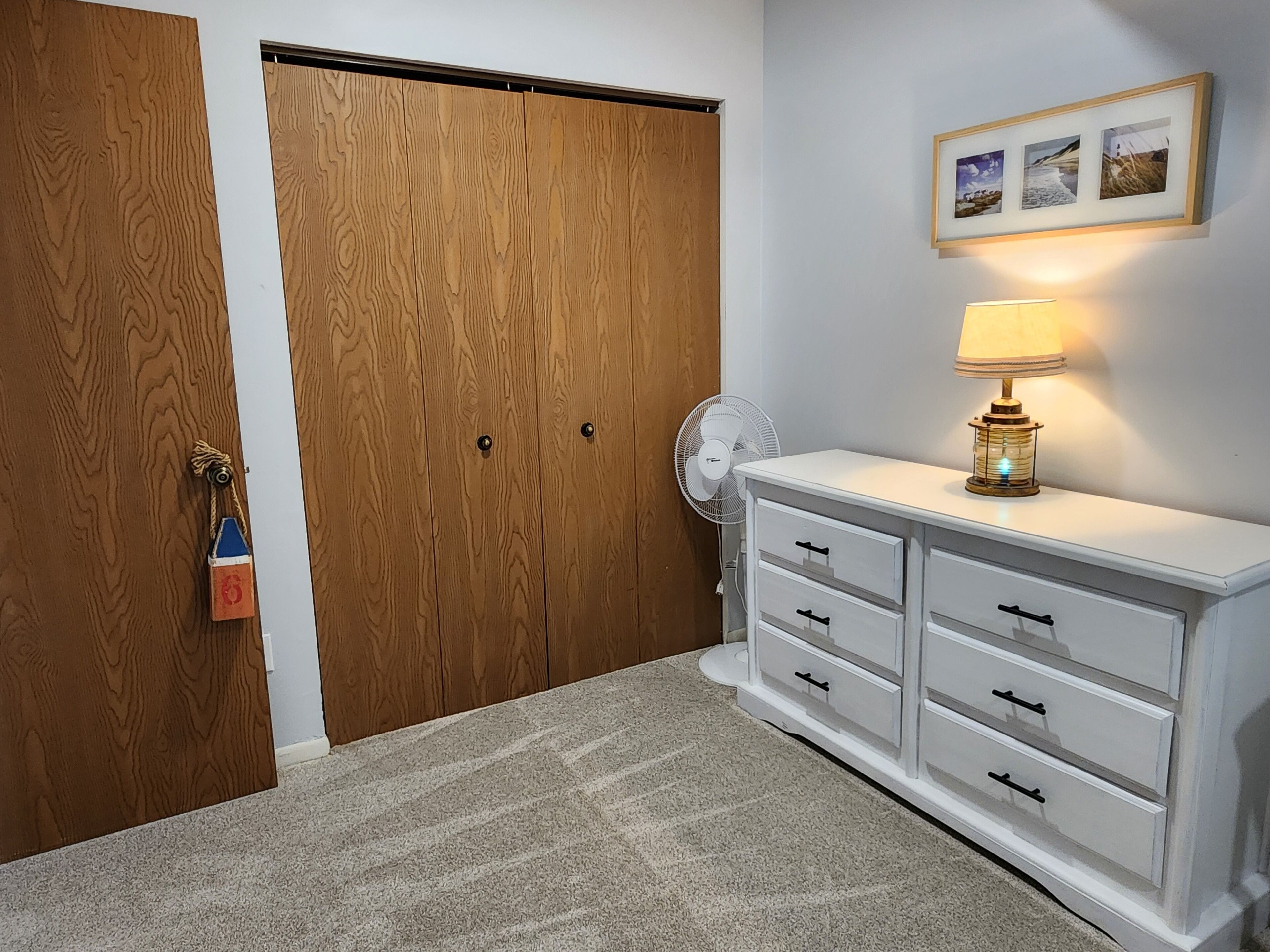 Ein Zimmer mit Holztür, einem weißen Kommode mit Schubladen, einem Ventilator und einer Wandlampe.