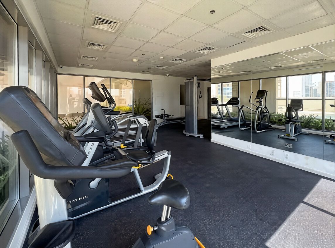 A gym with exercise equipment, large windows, and a view of buildings.