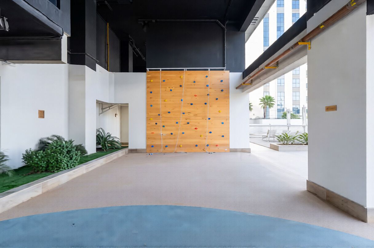A modern interior with a climbing wall, a blue carpeted area, and a white wall with a small plant.
