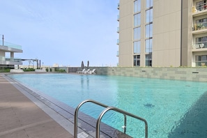 A swimming pool with a clear blue water, surrounded by a concrete deck and lounge chairs.