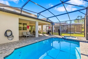 A pool area with a covered patio, lounge chairs, and a grill.