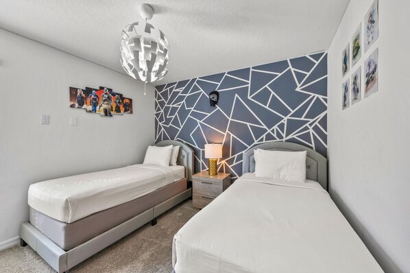 A modern bedroom with two beds, a geometric-patterned wall, and a unique ceiling light fixture.