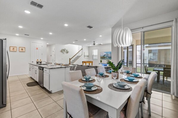 A modern kitchen with white cabinetry, a central island, and a dining area with a white table set for six.