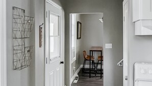 A hallway with a bench, a dining area with chairs, and a refrigerator.