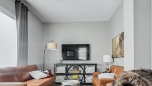 A modern living room with a ceiling fan, leather sofas, a flat-screen TV, and a large window with curtains.