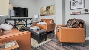 A modern living room with leather sofas, a flat-screen TV, and a large painting on the wall.