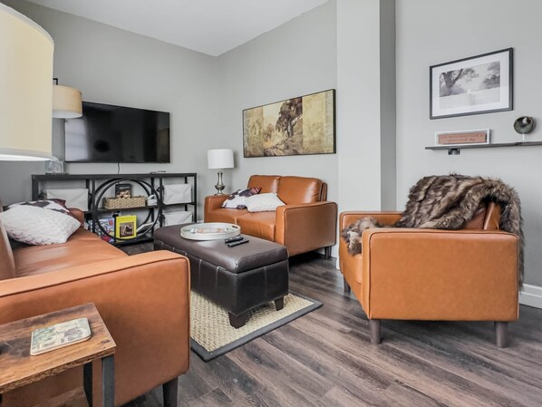 A modern living room with leather sofas, a flat-screen TV, and a large painting on the wall. - Walkerton Sauna Suite (Walkerton)