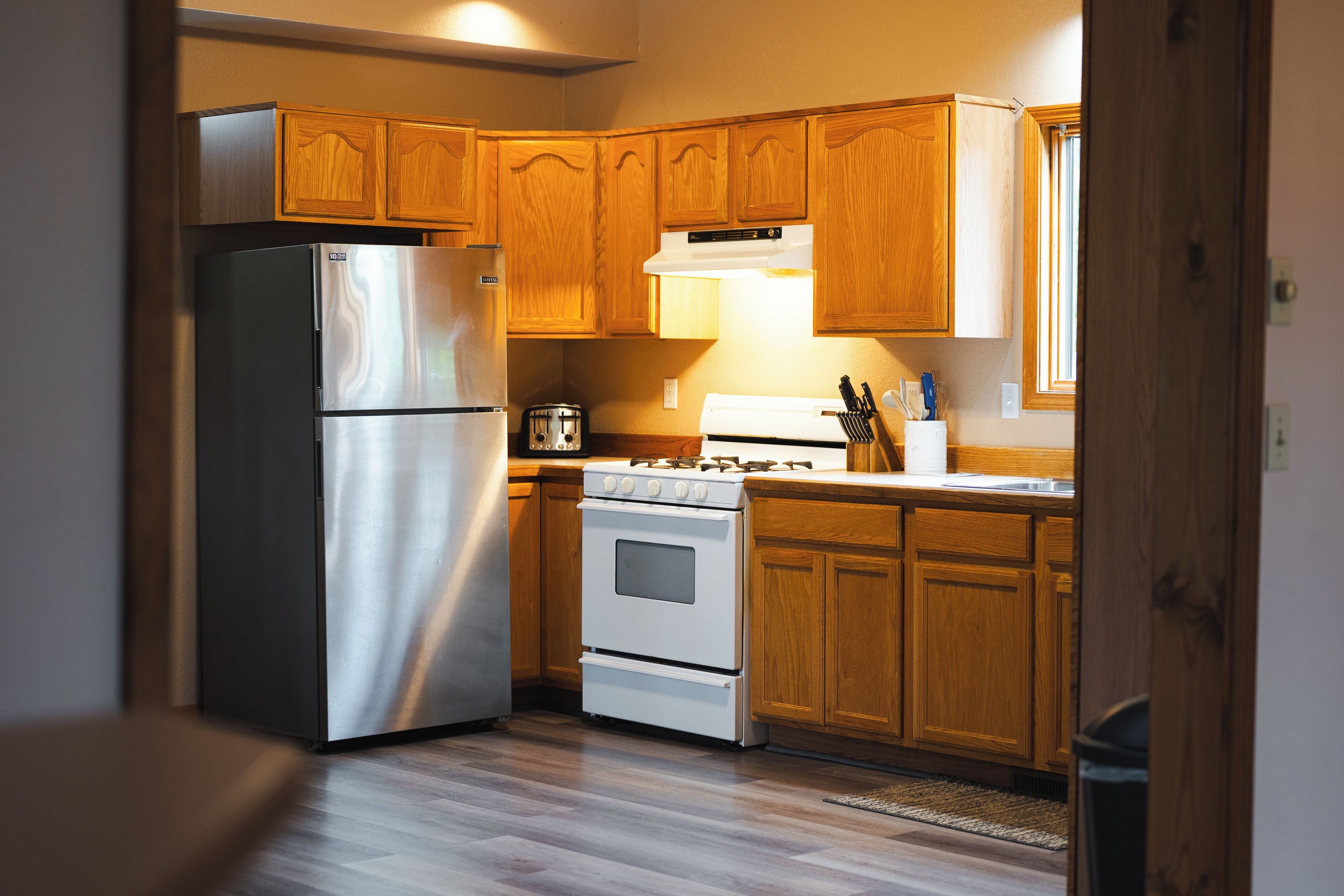 A kitchen with wooden cabinets, a stainless steel refrigerator, a stove, and a toaster.