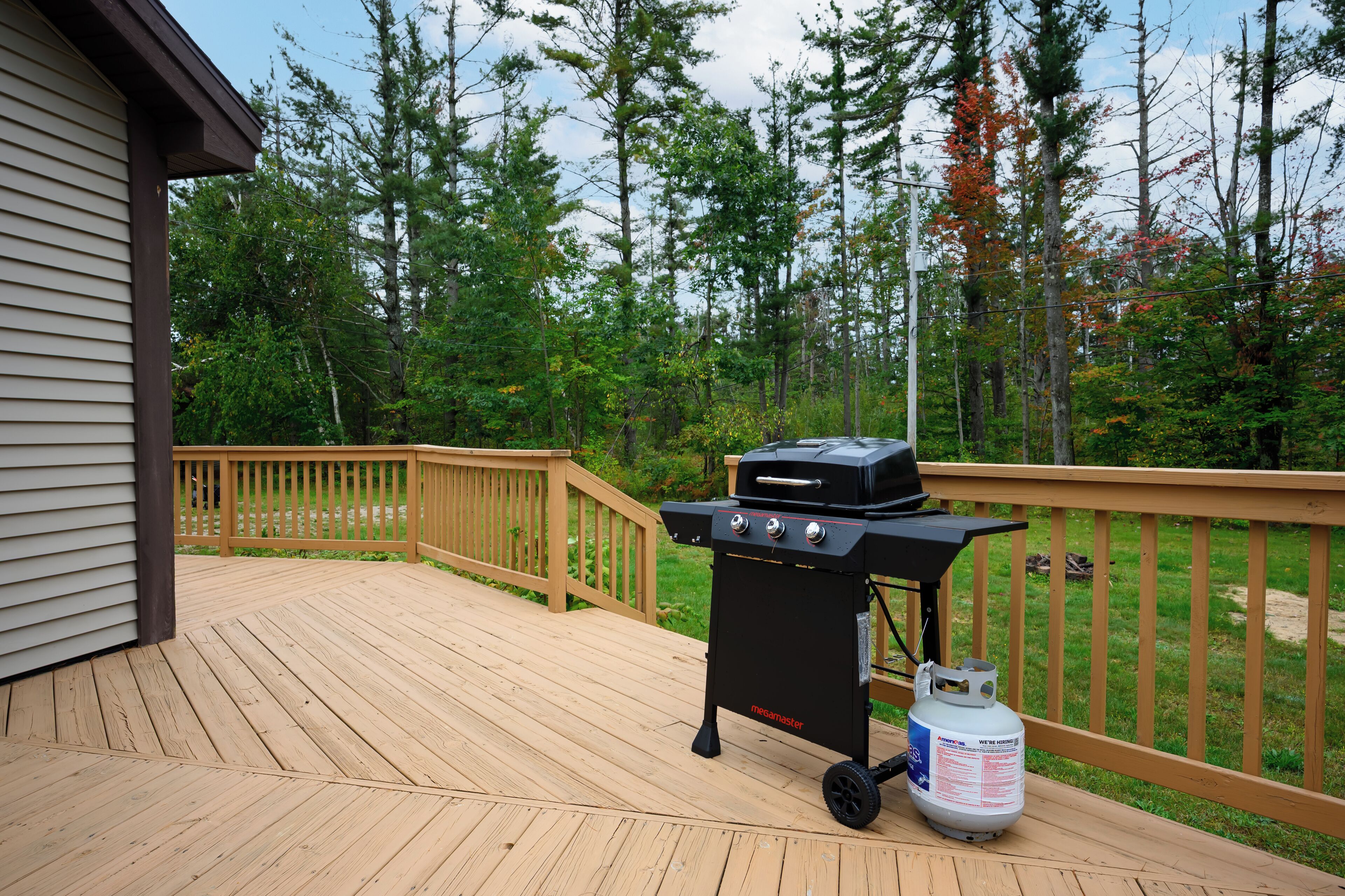 A deck with a barbecue grill and propane tank, surrounded by a wooden railing and trees.