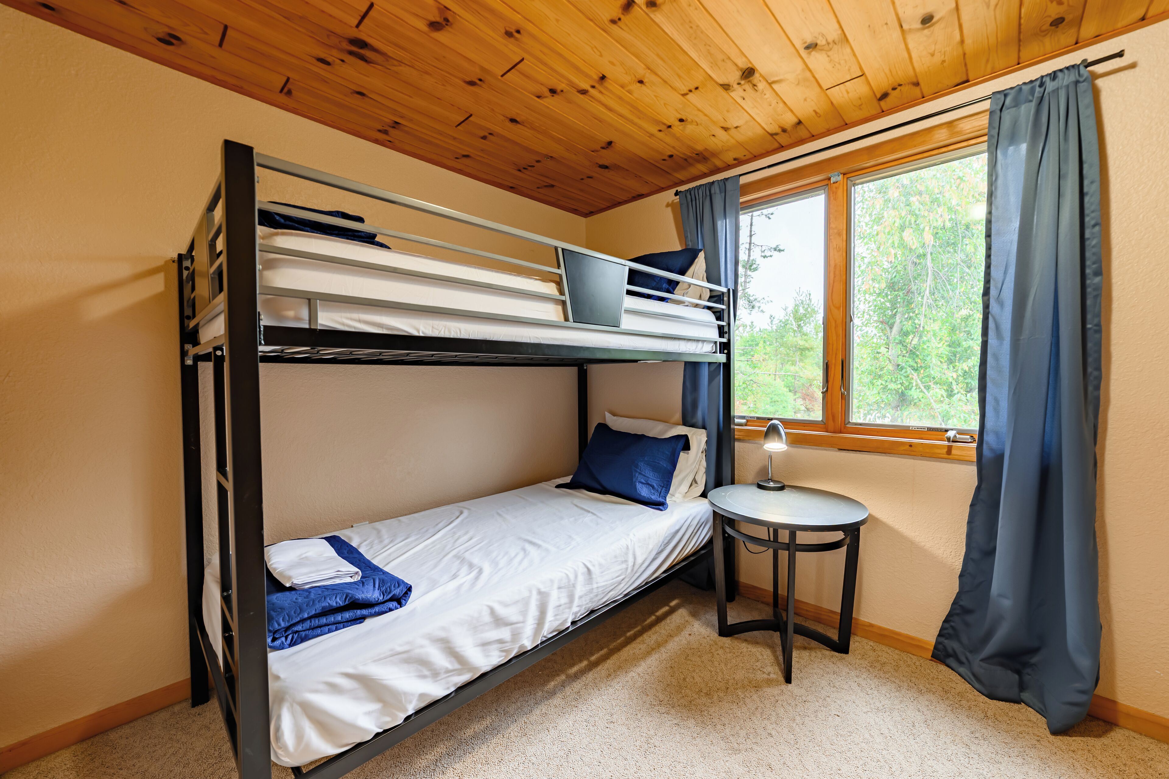 A bunk bed room with a small table and a window with curtains.