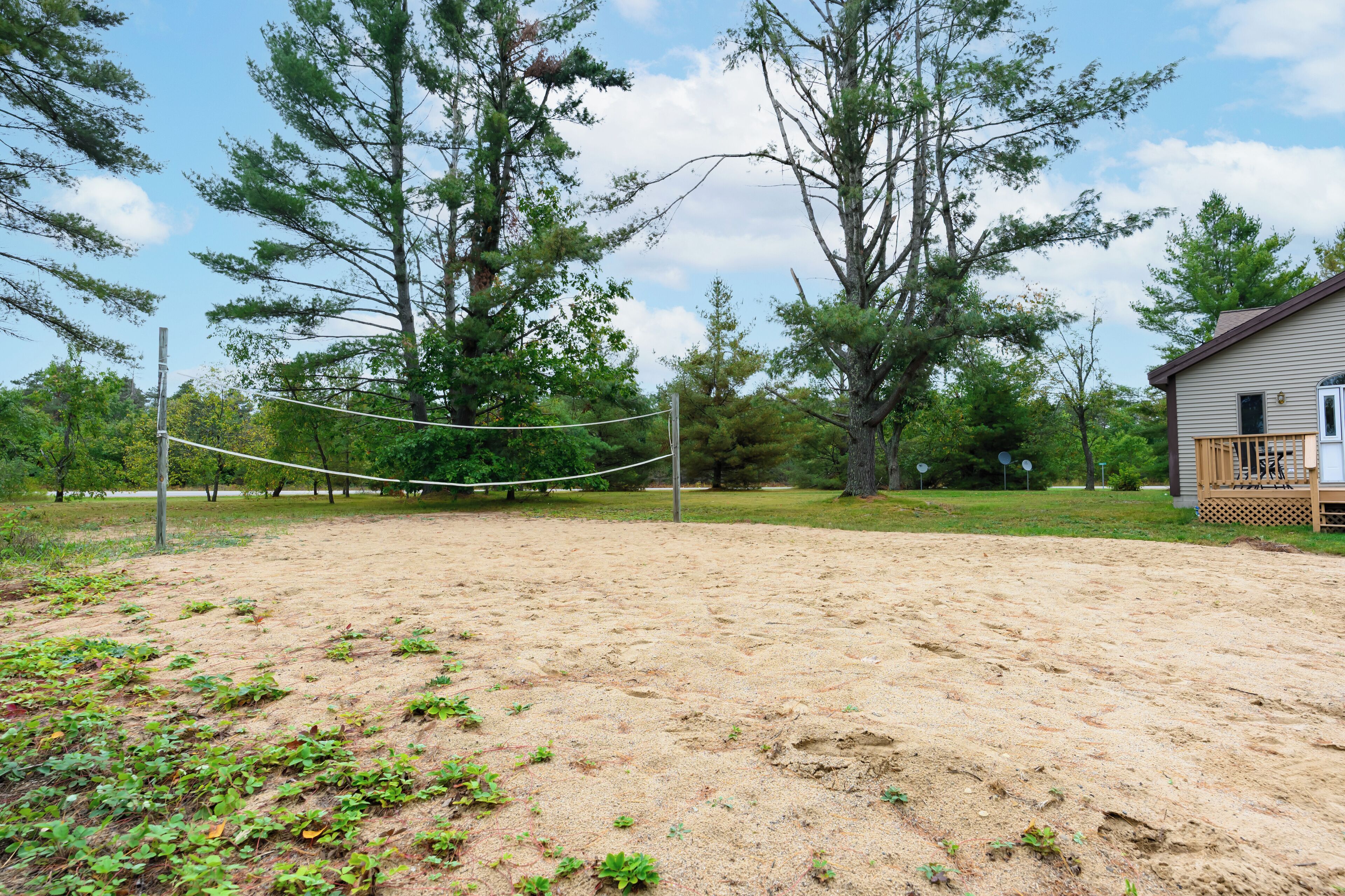 A volleyball net in a sandy area with trees and a wooden structure in the background.
