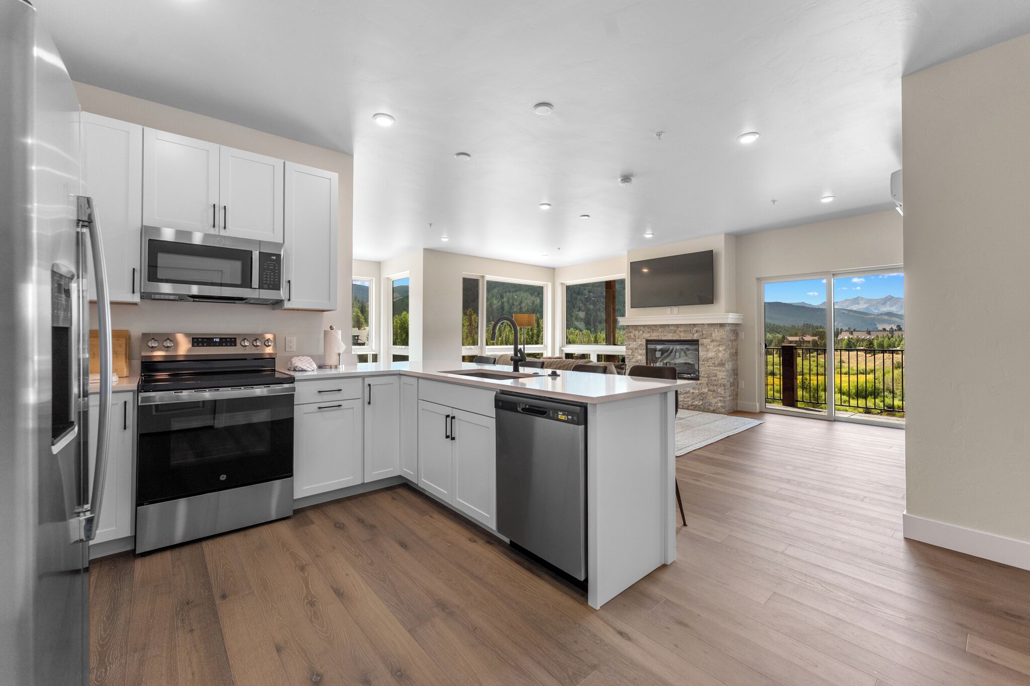 A modern kitchen with stainless steel appliances, a central island, and a large window overlooking a scenic landscape.