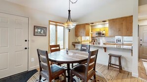 A dining area with a round table and chairs, a chandelier, and a kitchen with wooden cabinets and a microwave. - Peaceful Mountain View Home – Dog Friendly (Kalispell)