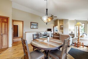 A dining area with a round wooden table, chairs, a hanging light fixture, and a ceiling fan.