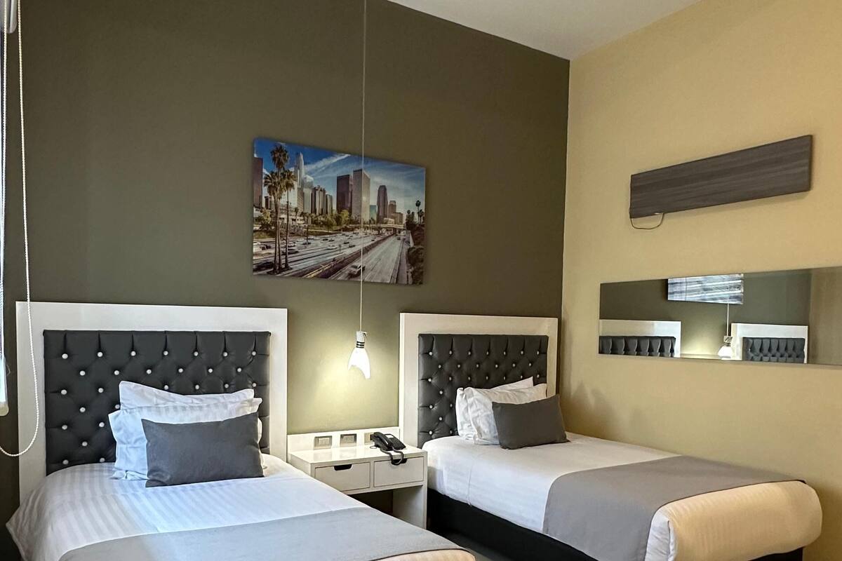 A hotel room with two beds, a cityscape painting, a nightstand, and a mirror.