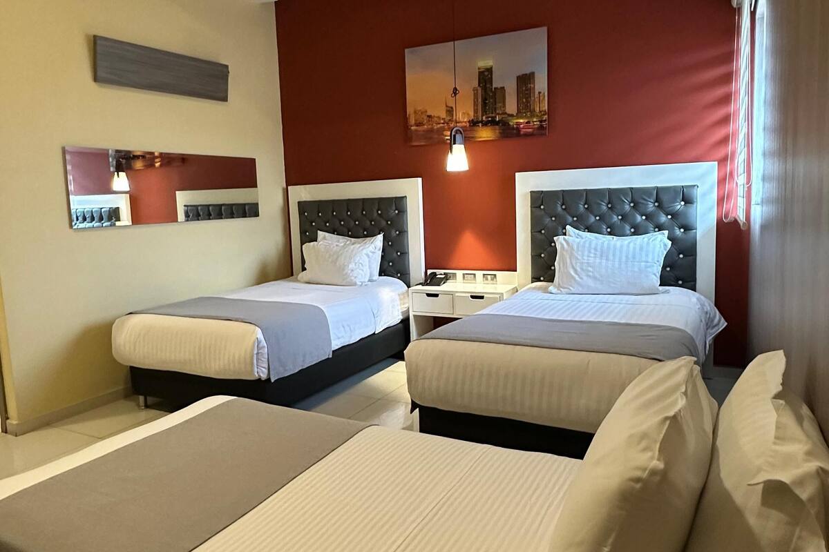 A hotel room with two beds, a cityscape artwork, and a modern ceiling design.