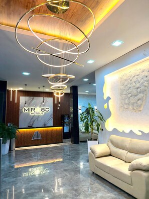 A hotel reception area with a modern design, including a marble reception desk, a sofa, and a unique wall art piece. - Mirago Hotel (Yumbo)