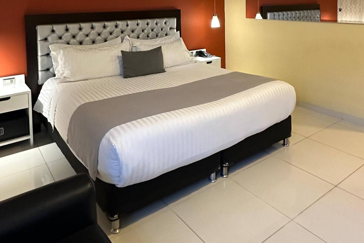 A modern hotel room with a large bed, a nightstand, a desk, and a chair.