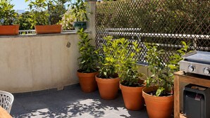 Een dak terras met potplanten, een barbecue en uitzicht op de skyline.
