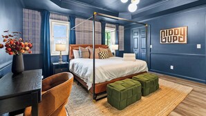 Une chambre à coucher avec un lit à baldaquin, un bureau agrémenté d’un vase de fleurs et un pouf vert.