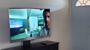A television on a dark wooden stand in a room with a patterned rug and a door labeled "HOME".