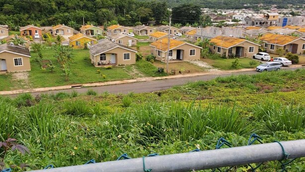 A residential area with houses arranged in rows, a road, and greenery in the foreground.