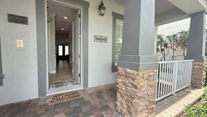 Entrada de una casa con un pilar de piedra, una verja metálica y un felpudo.
