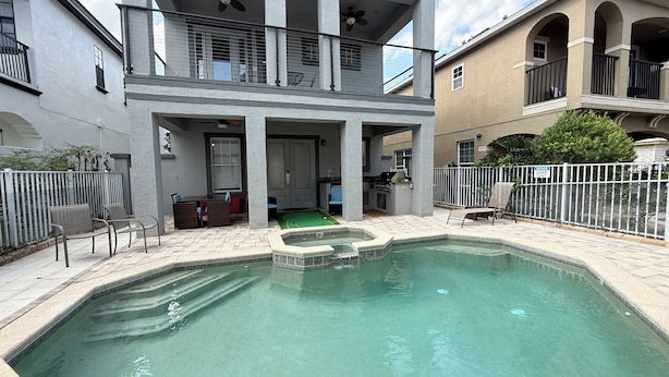 Un área de piscina residencial con un jacuzzi, asientos al aire libre y un porche cubierto.
