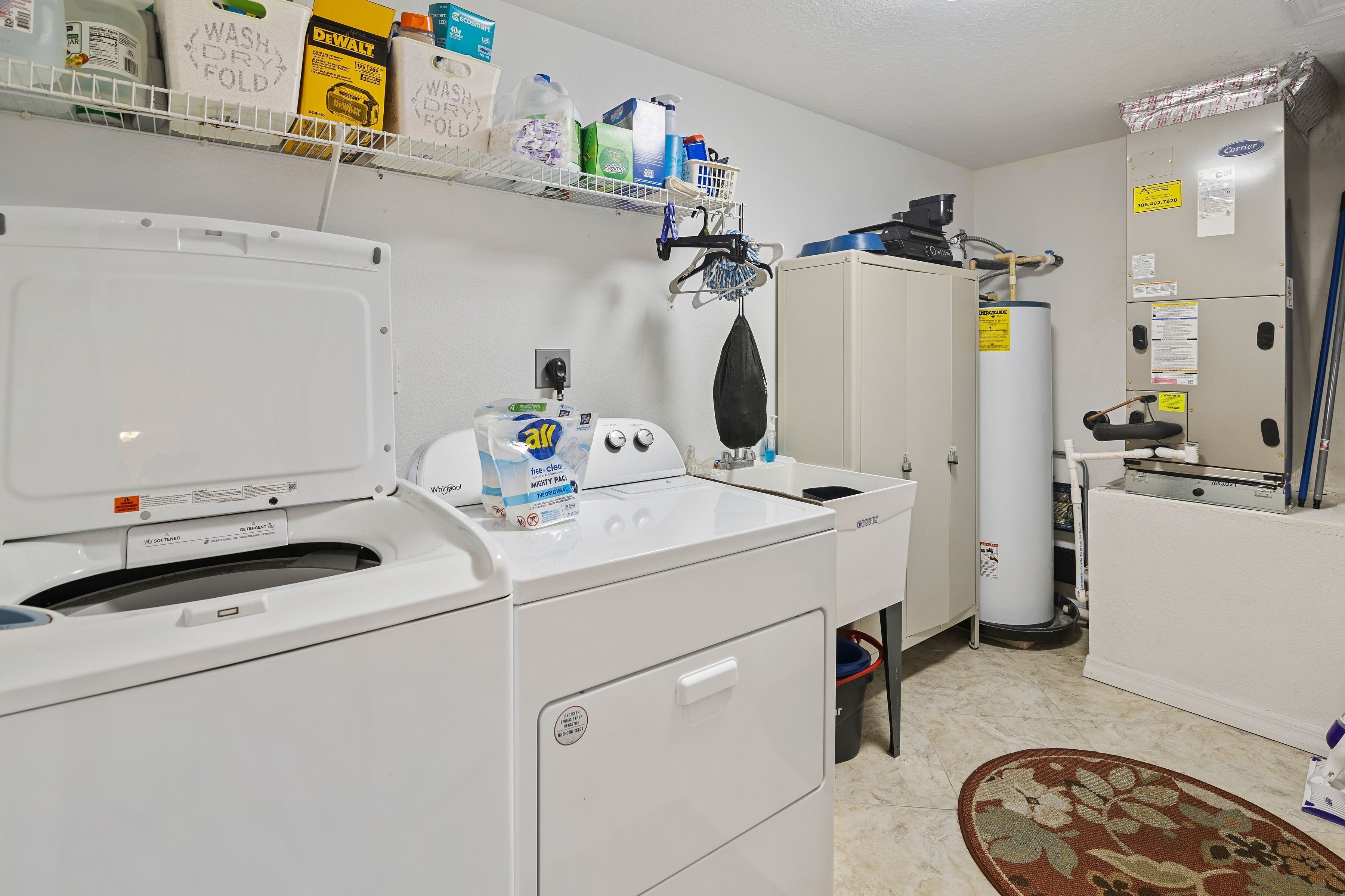 A laundry area with a front-loading washer and dryer, a water heater, and various cleaning supplies on shelves.