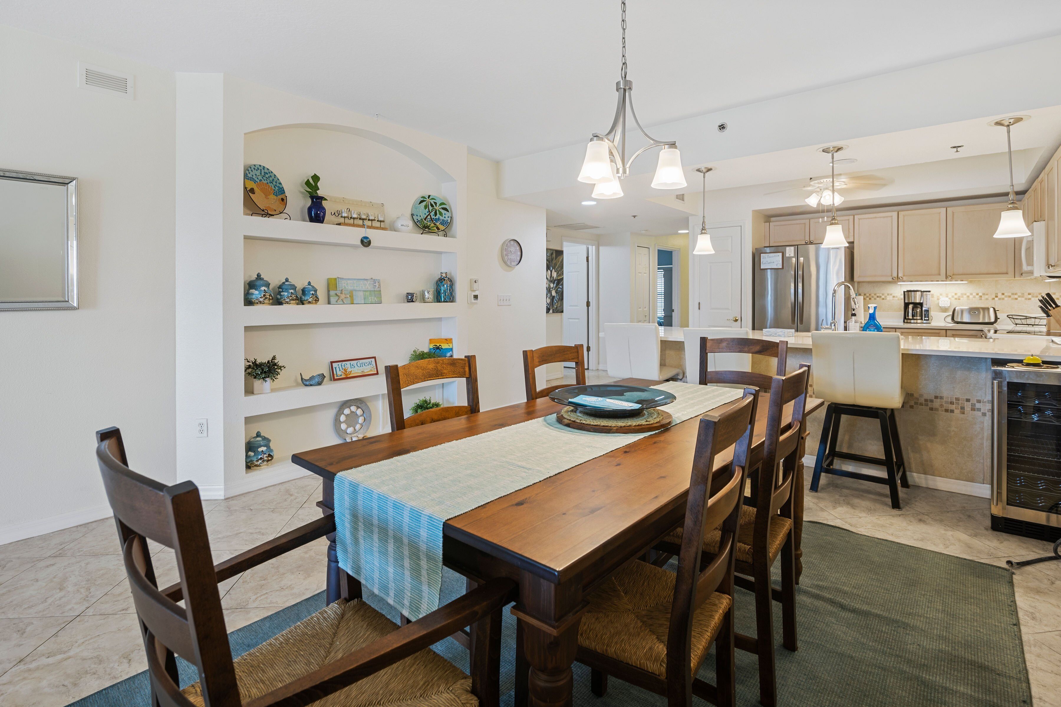 Un comedor con mesa de madera, sillas y una cocina al fondo.