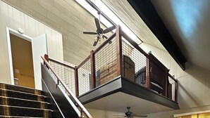 Una scala con ringhiera in legno che conduce a un balcone al secondo piano, dotato di parapetto.