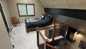 Ein Schlafzimmer im Spitzboden mit schrägem Dach, einem Bett, einem Sessel und einer Treppe.