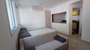 A modern hotel room with a sofa bed, a small kitchenette, and a TV mounted on the wall. - Pousada Village Maitinga (Bertioga)