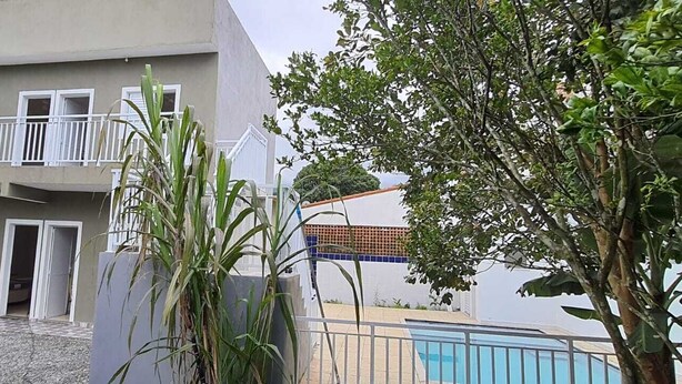 A two-story building with a balcony, a swimming pool, and a garden area. - Pousada Village Maitinga (Bertioga)