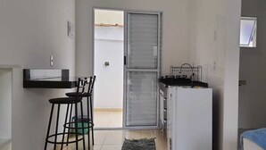 A compact kitchen with a refrigerator, a sink, and a bar stool. - Pousada Village Maitinga (Bertioga)