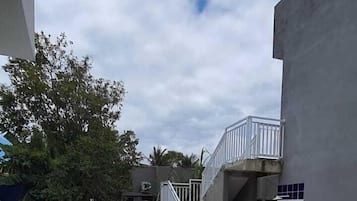 Piscina com piso azulejado, escadaria para uma varanda e um edifício com fachada cinzenta.