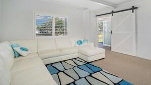 A white sectional sofa with blue pillows, a patterned rug, and a sliding barn door. - Beverley Beach - Whangamata Holiday Home (Whangamata)