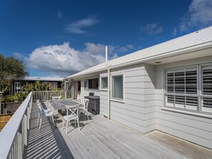 Ett vitt hus med en träveranda, ett matbord med stolar och ett litet utomhuskök.