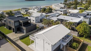 A residential area with modern houses, a large white building with a balcony, and a view of the sea and a small island. - Beverley Beach - Whangamata Holiday Home (Whangamata)