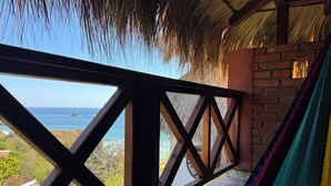 A hammock on a balcony with a view of the ocean and a thatched roof.